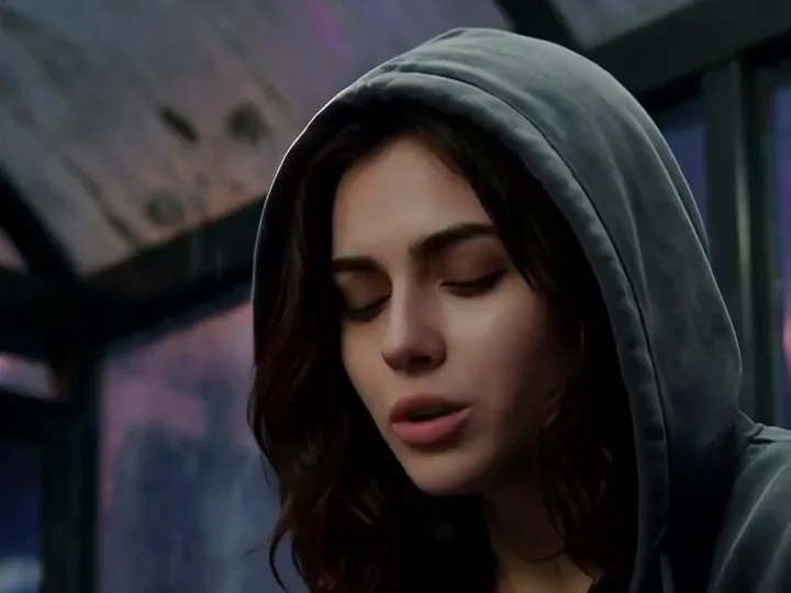 AI Singer video frame: close on a woman in a grey hood singing at a rainy bus stop, her lips on the words